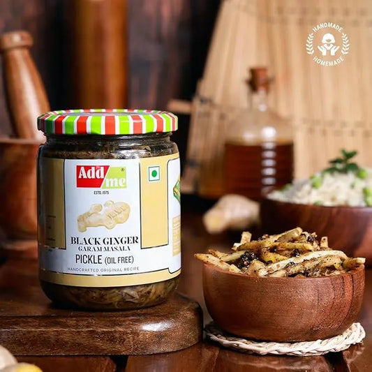 Jar of Addsome black ginger garam masala pickle on a wooden surface with a bowl of pickles in the background.