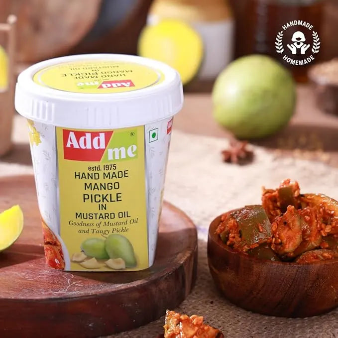 Add me hand made mango pickle in mustard oil with a bowl of pickle and lemon slices on a wooden surface.