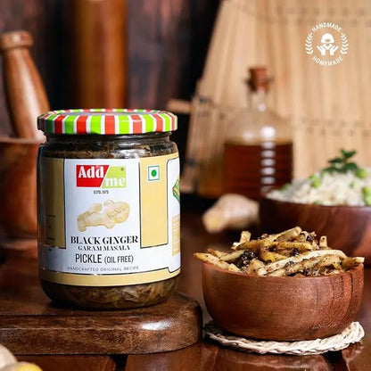 Jar of Addsome black ginger garam masala pickle on a wooden surface with a bowl of pickles in the background.