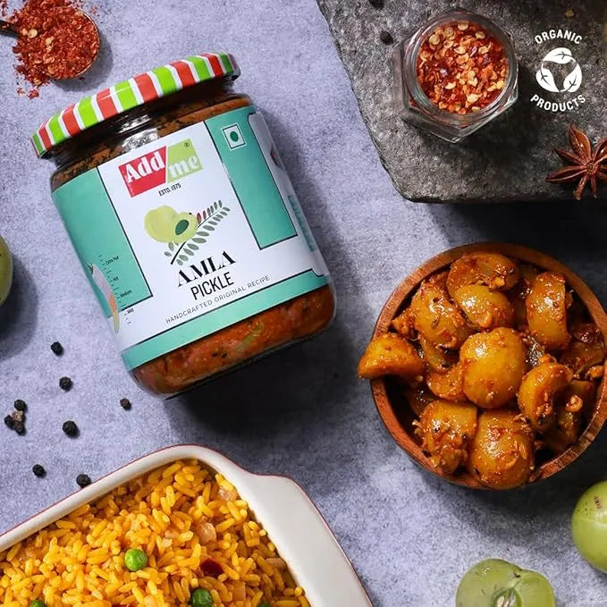 Jar of Amla pickle with a bowl of food and spices on a gray surface