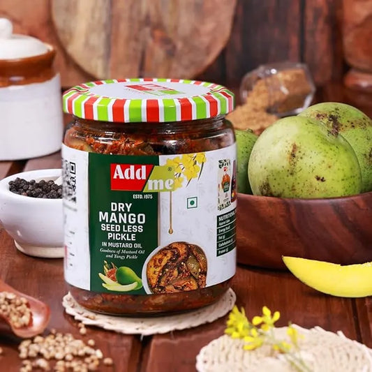 Jar of Add Some Dry Mango SeedLess Pickle on a wooden table with mangoes and spices.